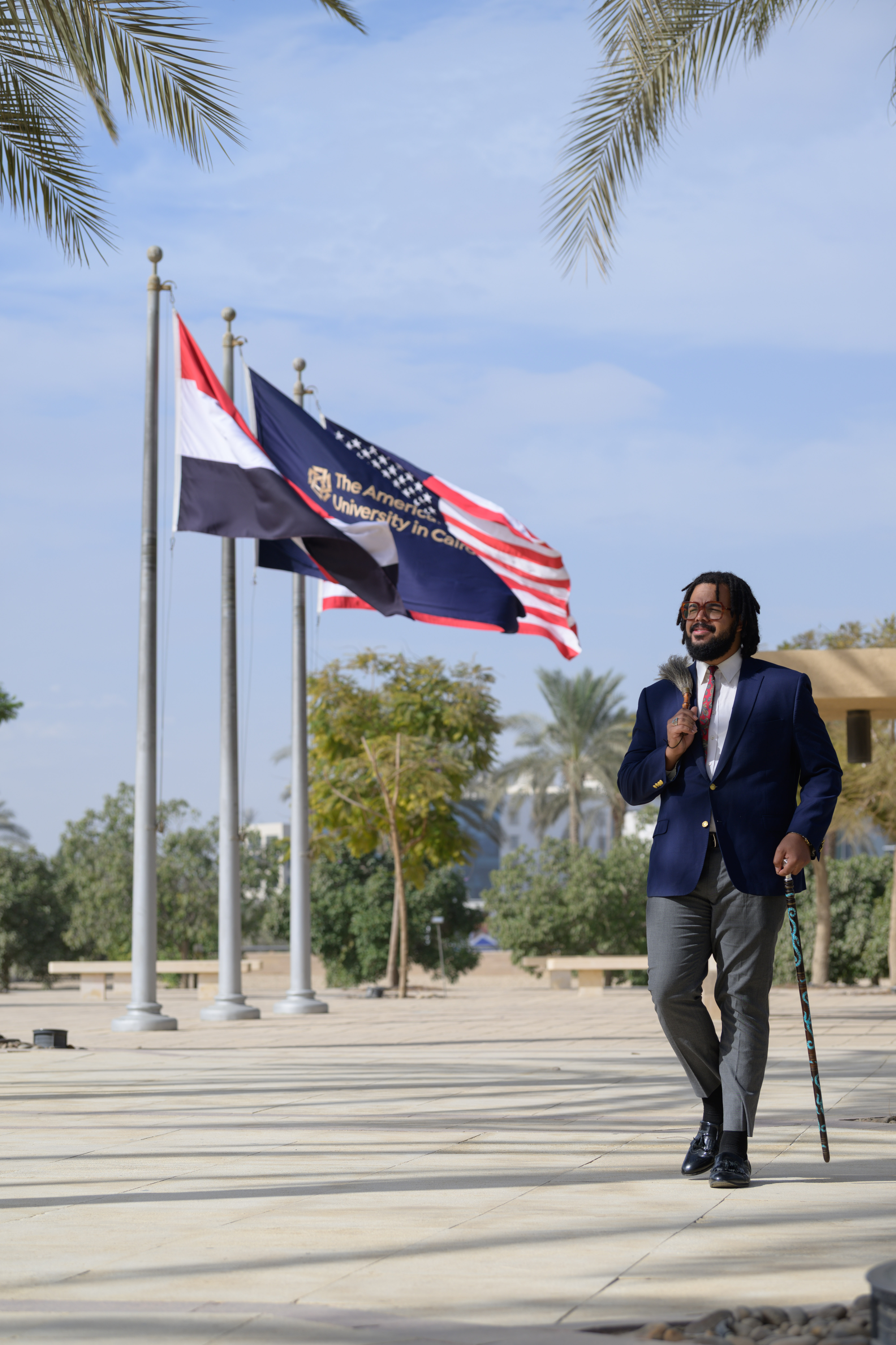 Seneca Forch walks outside with a cane while the Egytian, AUC and American flags fly in the background