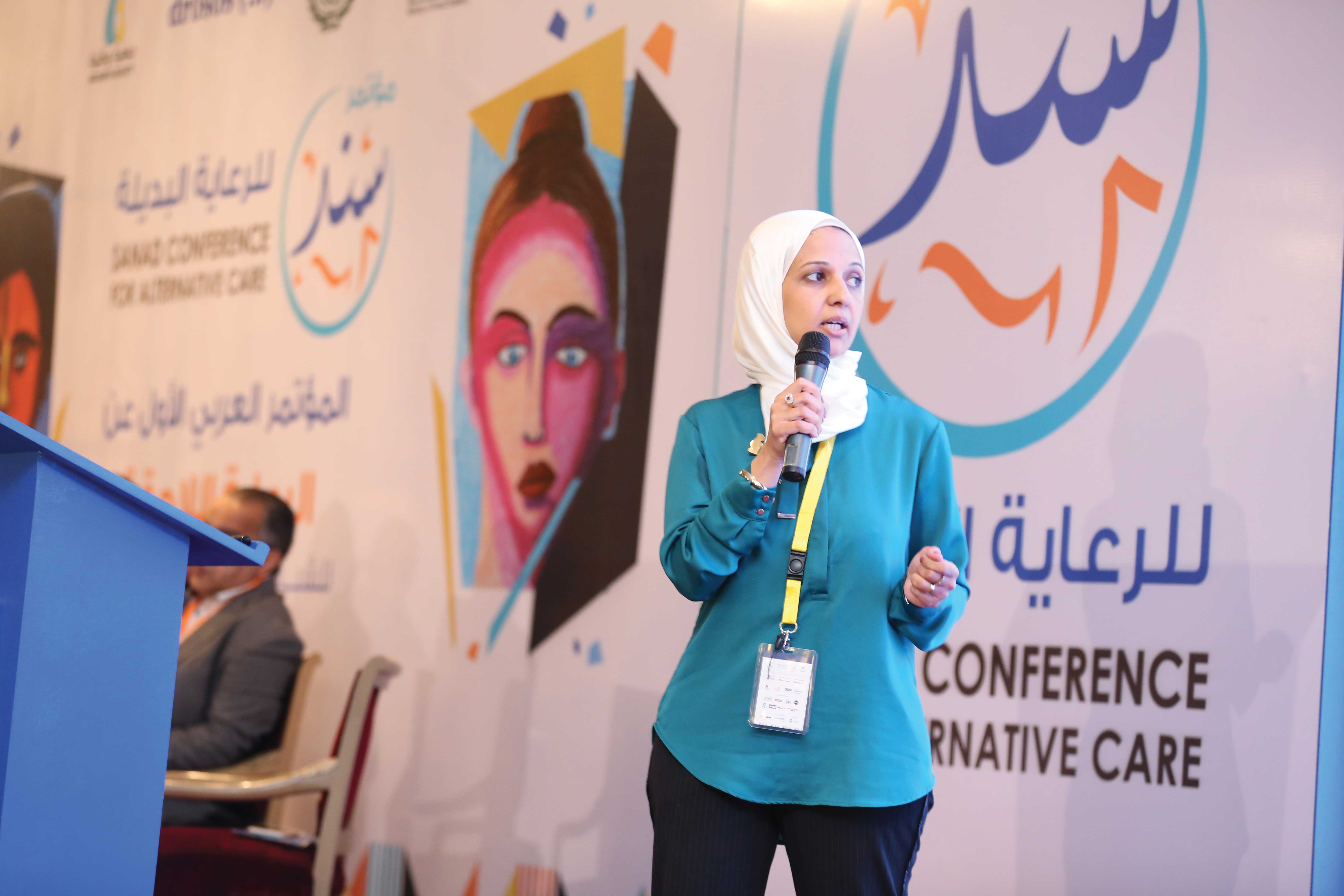 Yasmine El Hagry speaks at a podium holding a microphone and standing.