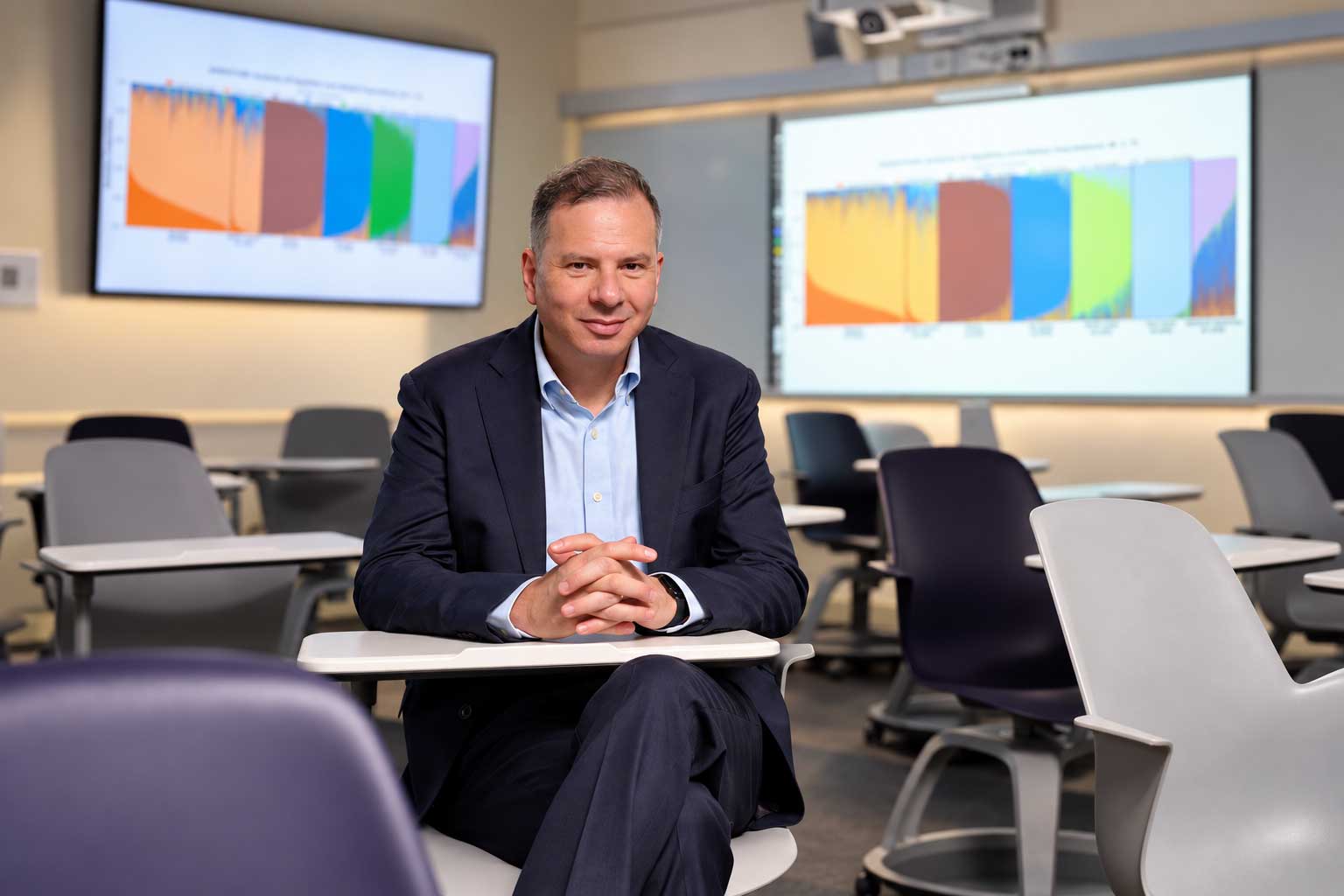 Professor Ahmed Moustafa sitting in a classroom with screens around him