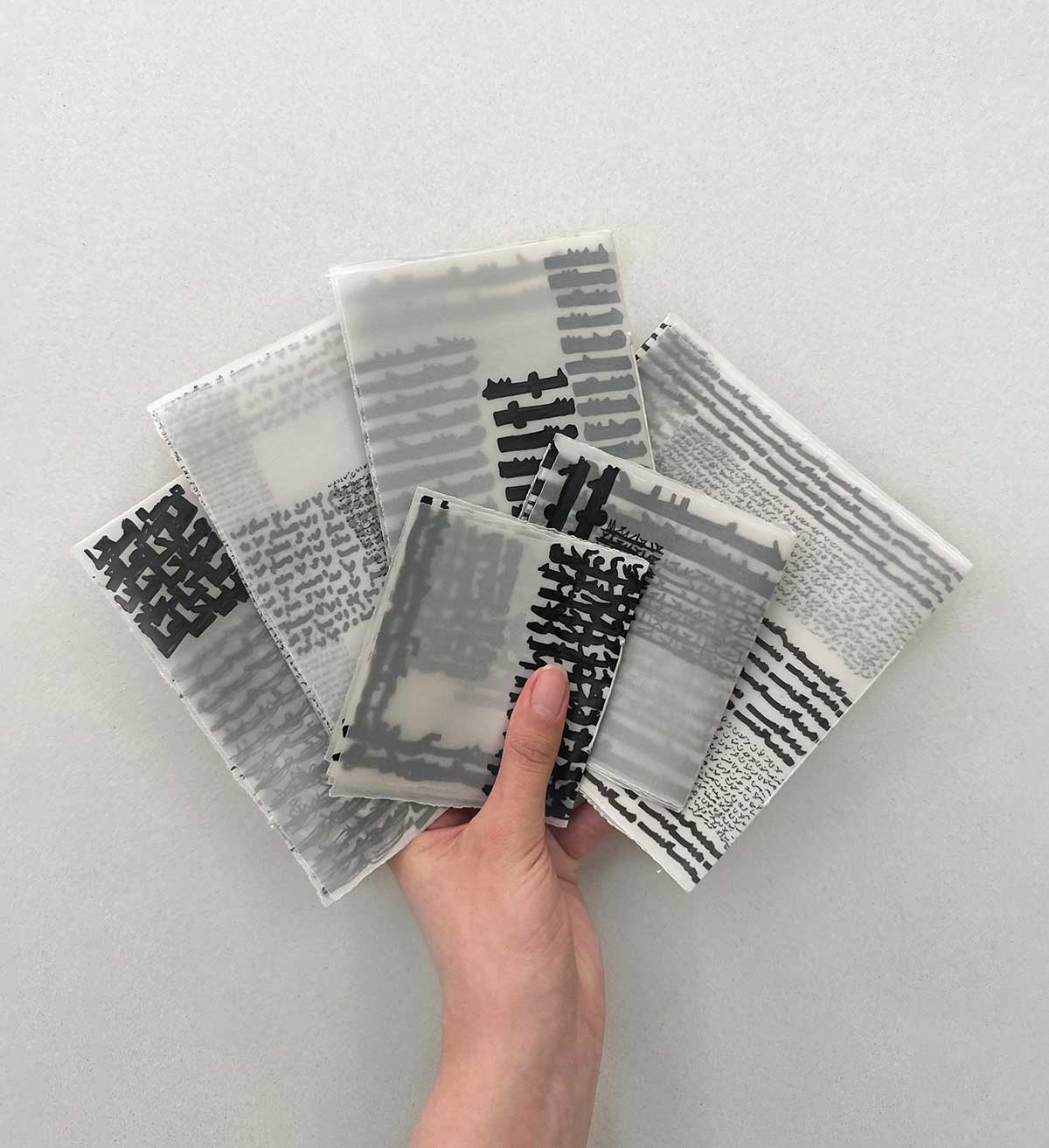 A hand holds six folded pieces of fabric which are each covered in stylized Arabic script