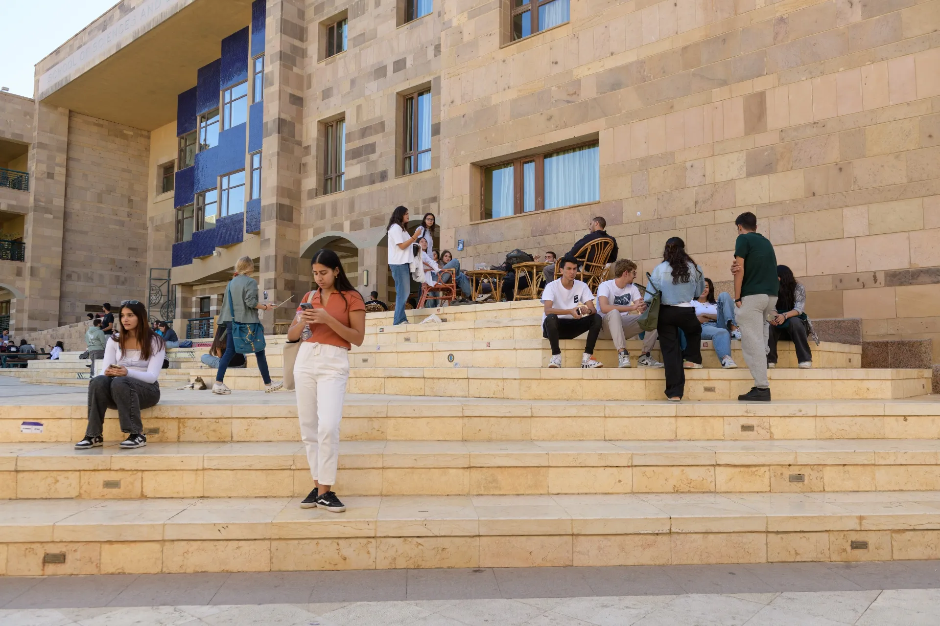 a woman stands on a set of stairs in front of AUC's Sciences and Engineering Building, looking at her phone