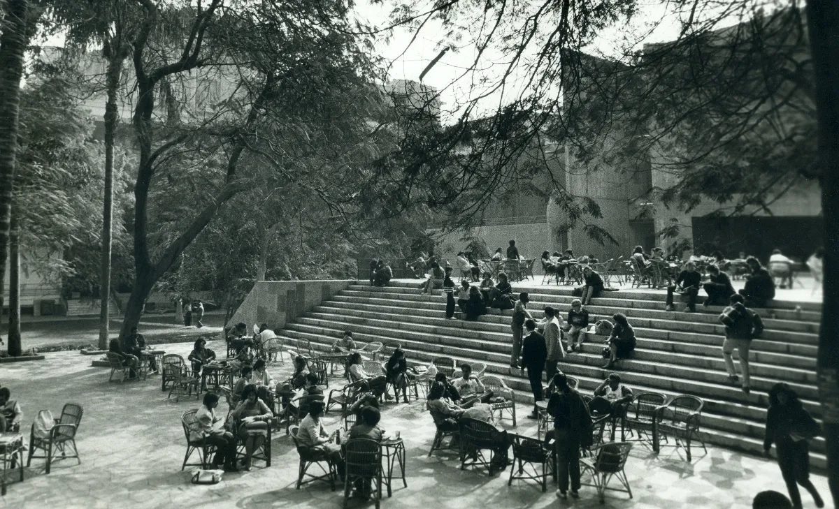 a black and white photo of a large set of stairs with students sitting on them and table and chairs in the foreground