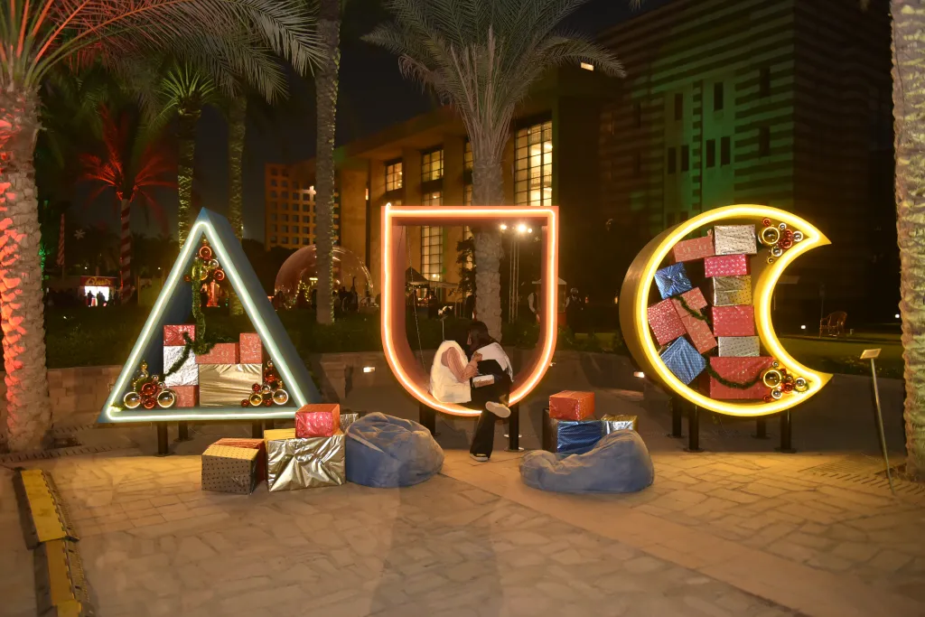 AUC sign lit up by Christmas lights with wrapped presents scattered in the foreground