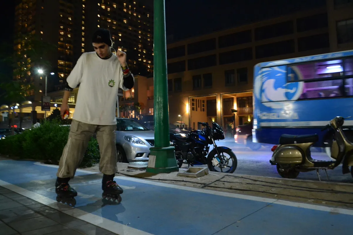 a man skates backwards on the corniche at night while a bus and cars drive by in the background