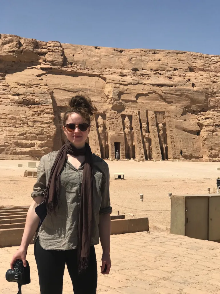 woman stands with a camera in front of a temple in Egypt