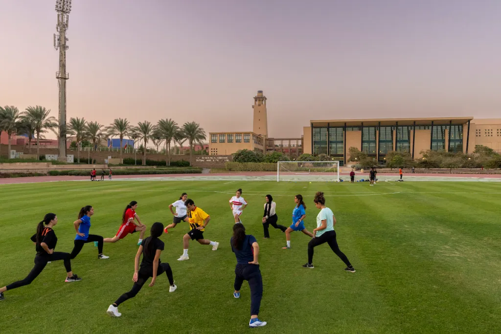 Athletes stretch in a circle at the field next to the AUC sports center
