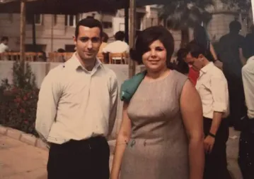 A couple stands smiling at the camera in a vintage photo.