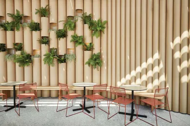 A wall made of paper tubes, with plants fit into it and several tables with chairs in front. 