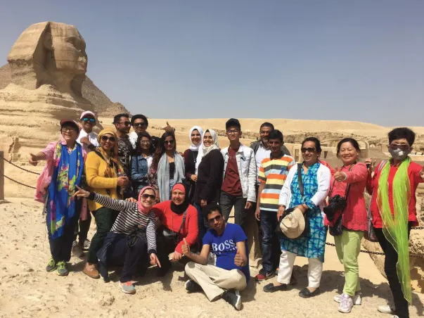 A group of students standing in front of the Sphinx statue in Egypt giving thumbs up and smiling.