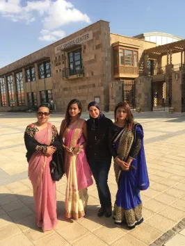 Three women in saris with a woman in jeans standing in front of AUC's Sports Center building smiling