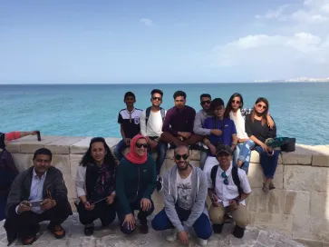 A group of Egyptian and Nepali students sitting on a stone wall in front of the sea