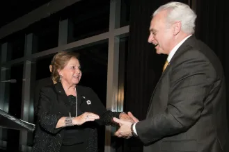 A woman in a black dress shakes hands with a man as they both smile