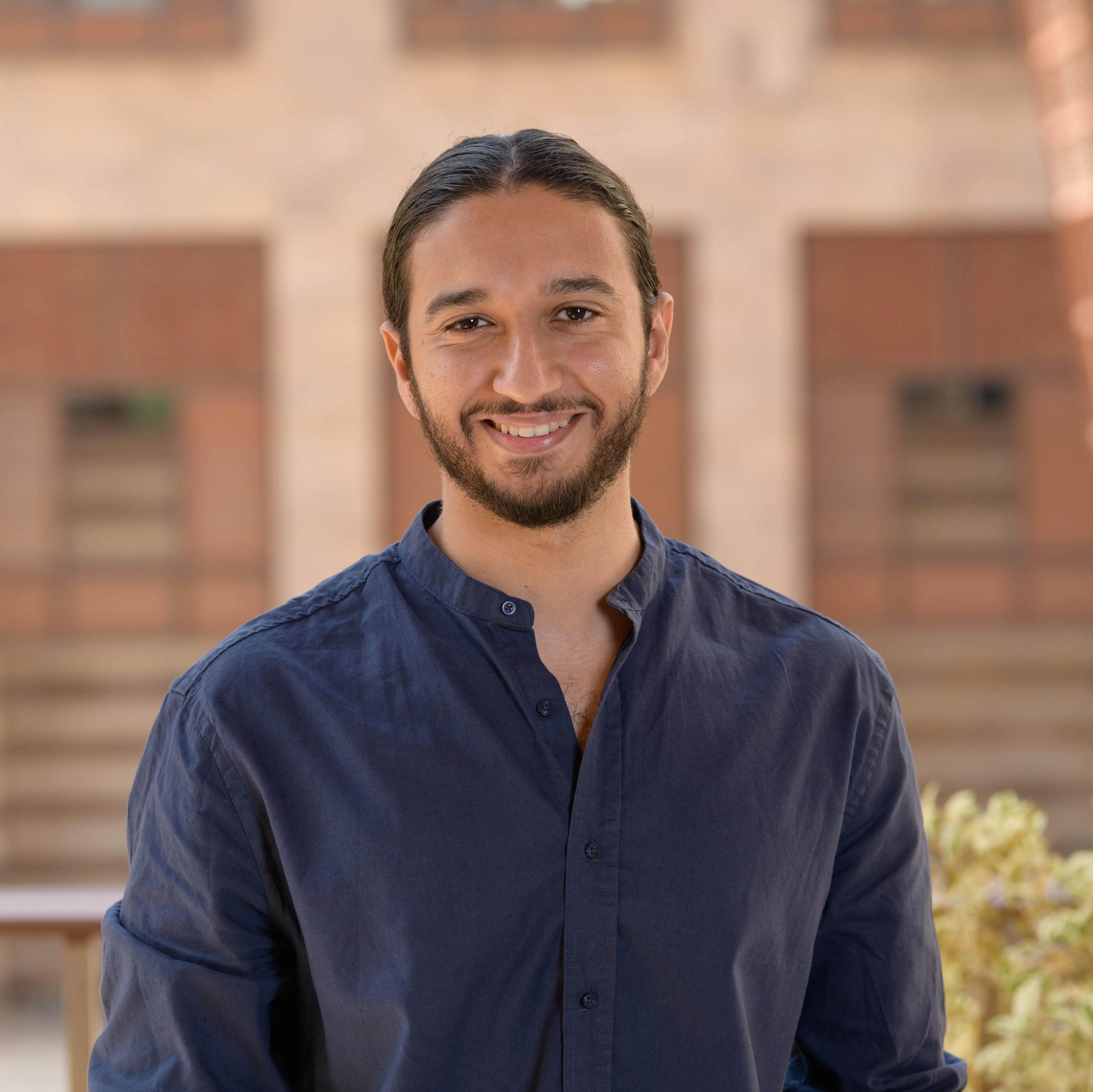 man wearing a blue shirt smiling, standing in front of a building at AUC New Cairo