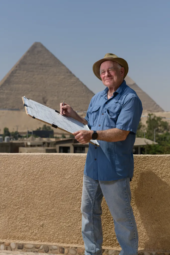 Man standing in front of the Pyramids of Giza holding a clipboard and a pencil with a map on it